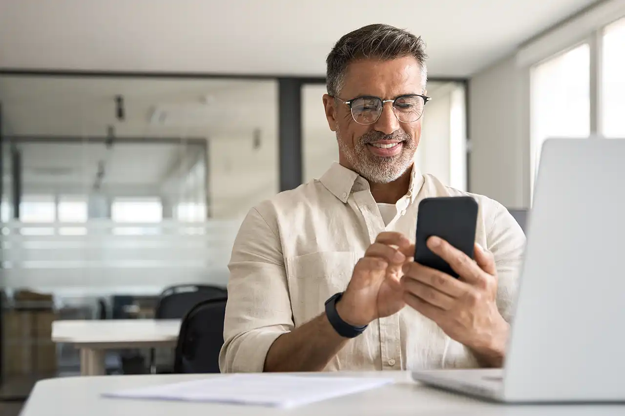 Business professional using a smartphone beside a laptop in an office